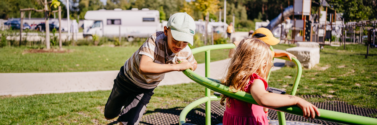 Kinder spielen auf einem Karussell, eines sitzt drinnen, das andere Kind schiebt es von außen an.